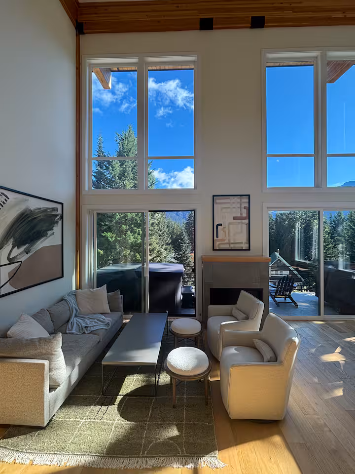 Sunlit living room with tall windows and forest views